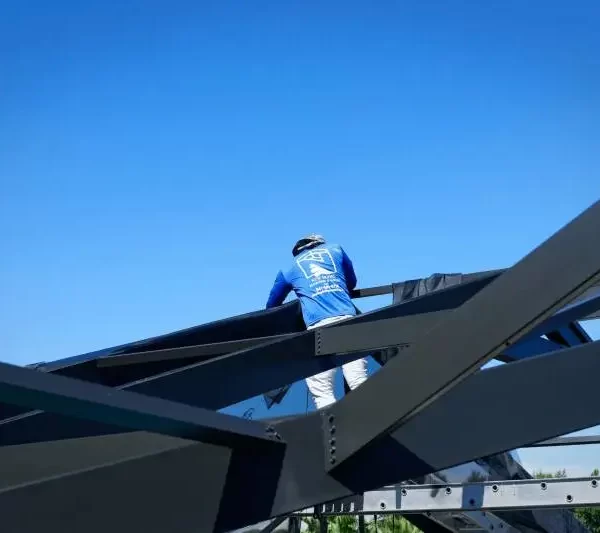 Technician in blue uniform working on the restoration of a pool cage structure under a clear blue sky, showcasing professionalism and safety standards.