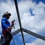 Worker restoring and rescreening a pool cage structure under a blue sky.