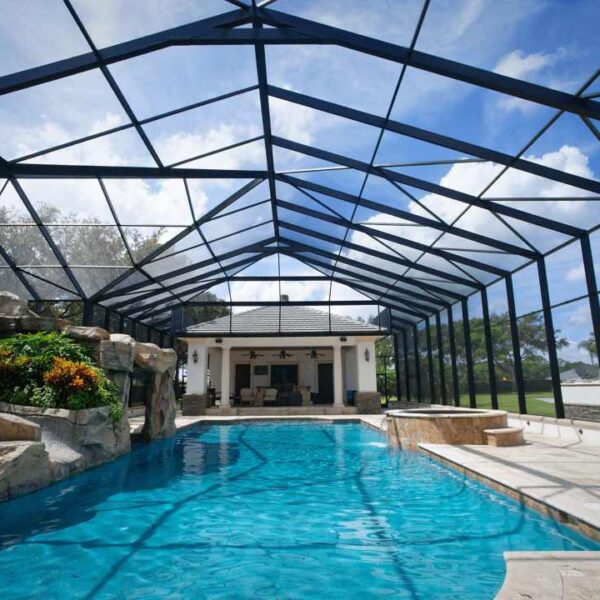 Beautifully restored pool cage enclosure with a luxurious pool and rock garden under a clear blue sky.
